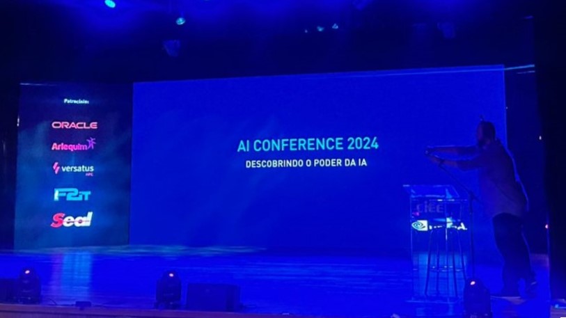 Palco da AI Conference 2024, com o telão exibindo o nome do evento, momentos antes de uma das apresentações.